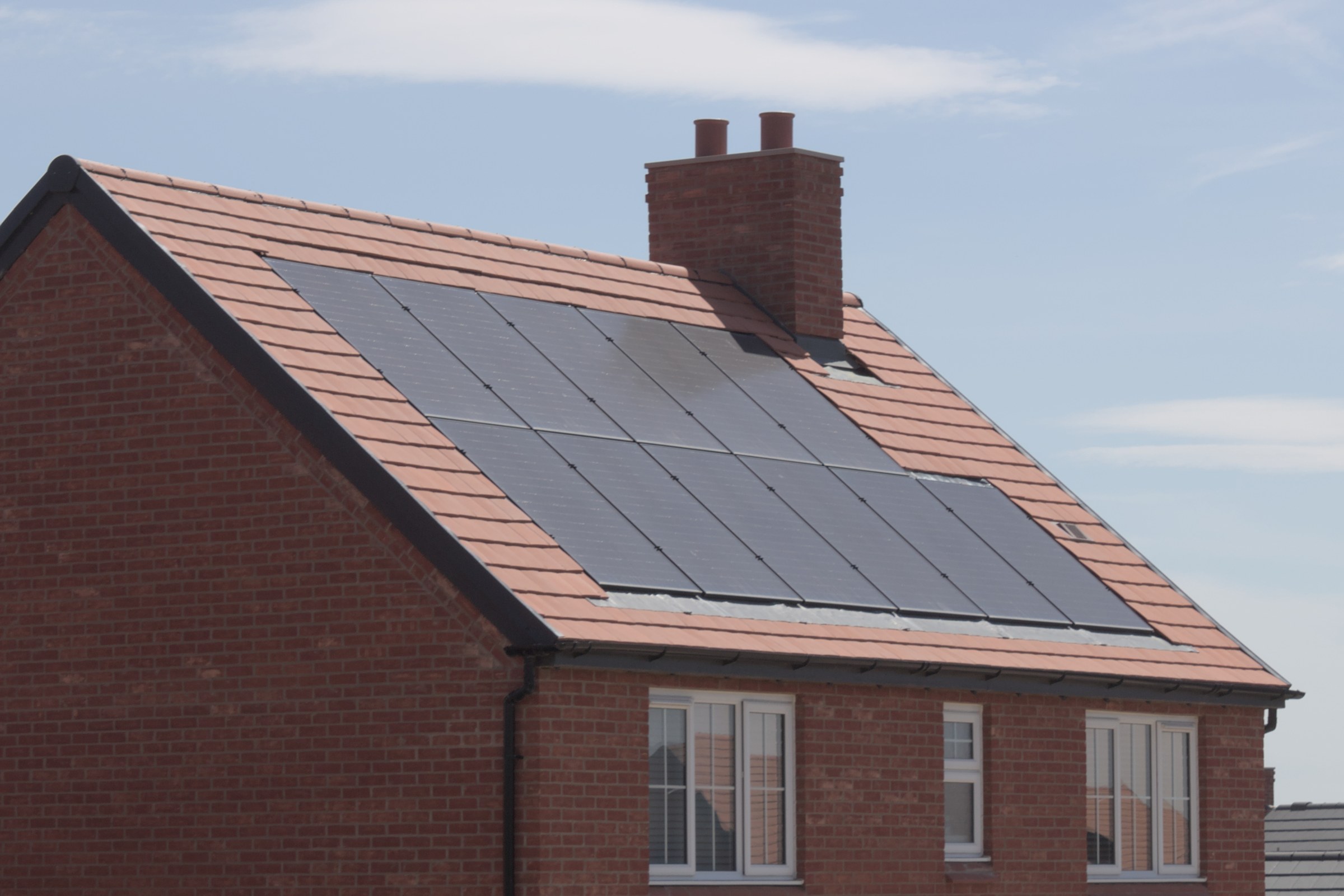 Red-brick home with all-black solar panels on a tiled roof